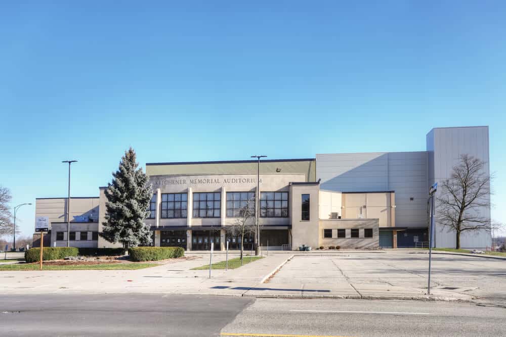 An image of Kitchener Memorial Audiotorium Ontario. It shows a large beige building with a tree in front of it