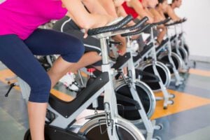 An image of a spin class. It shows the bottom legs of several people sitting on stationary bicycles